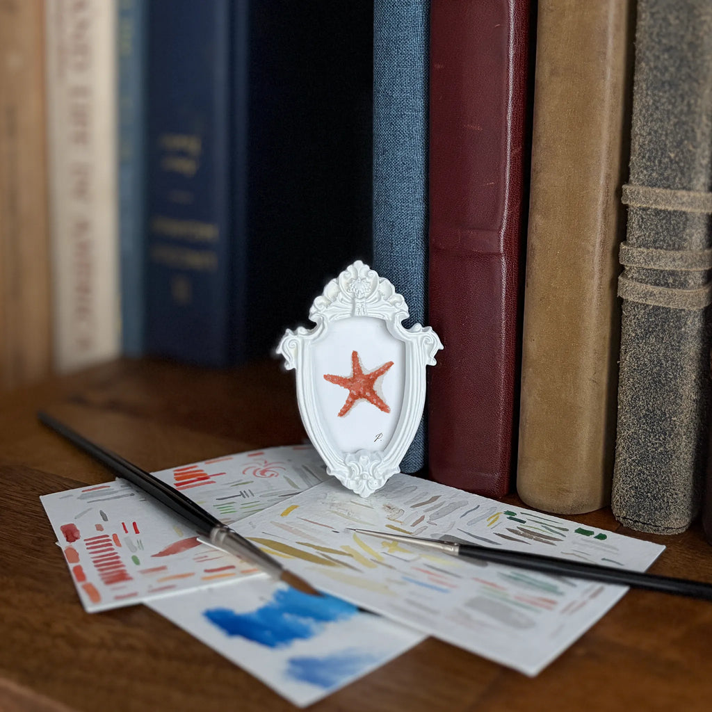 Art fairy magic themed books with a white ornate frame holding a red star on a table