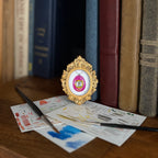 Art and Magic fairy pendant in an ornate gold frame resting on colorful cards beside books