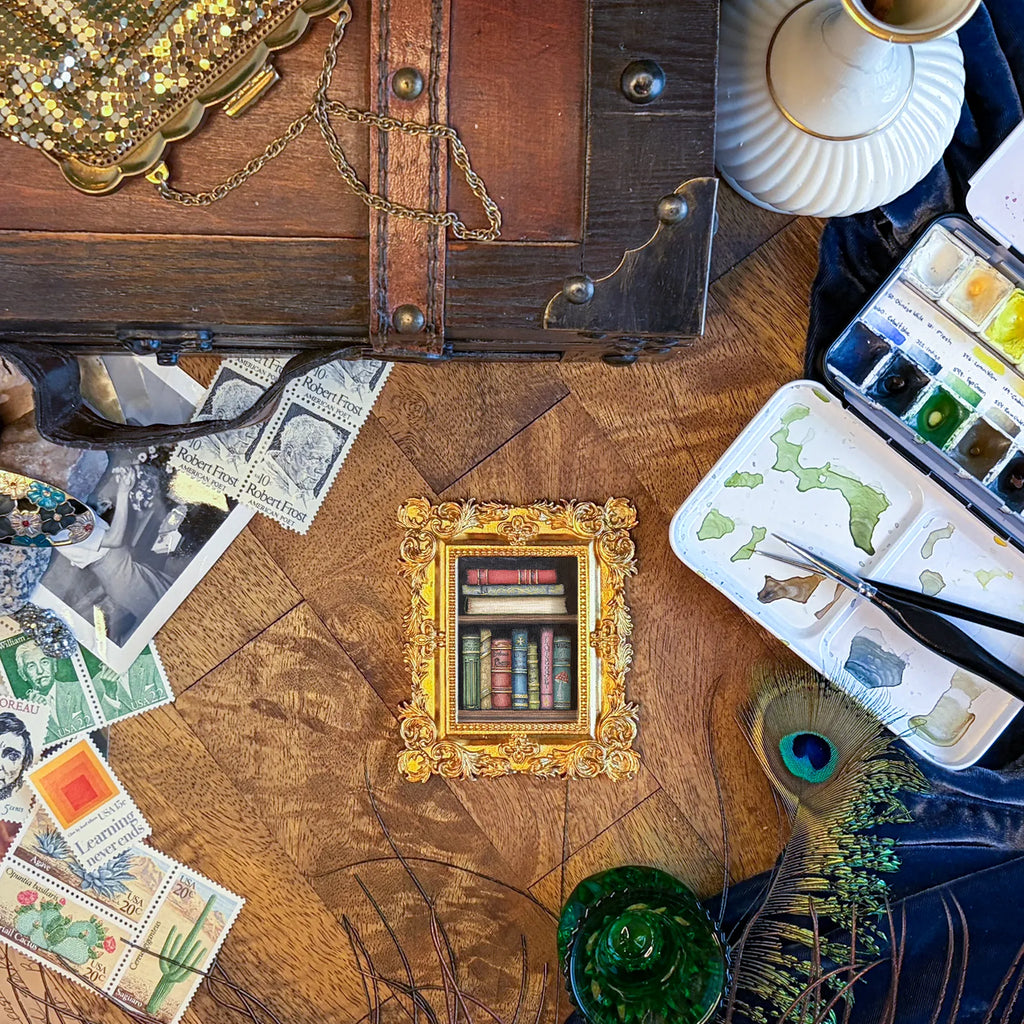 Art supplies on a wooden table, including a fairy magic themed frame, stamps, and paint tubes.