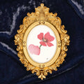 Art fairy magic in a gilded oval frame with pink flower paint on a dark blue fabric background