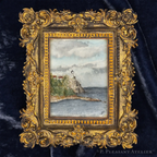 A miniature framed art piece featuring a hand-painted lighthouse scene on a rocky coast, set within an ornate gold frame and displayed on a dark navy velvet background.
