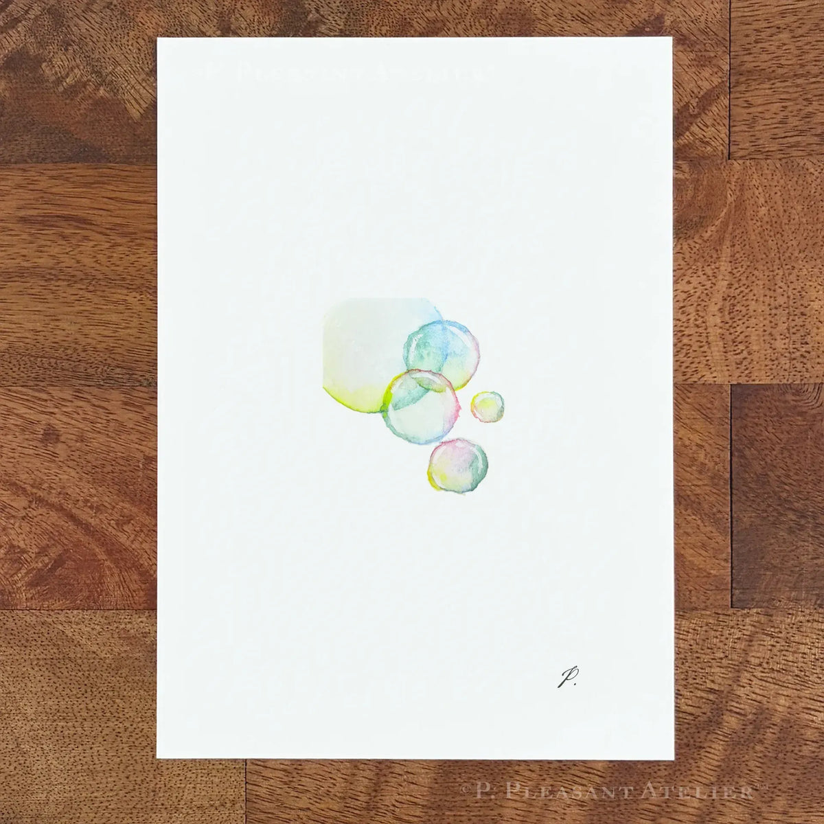 A vertical watercolor art print featuring a cluster of translucent bubbles in pastel shades of blue, green, and yellow on a white background, displayed flat on a brown wooden surface.