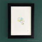 Framed minimalist art print featuring a cluster of translucent watercolor bubbles on a white background, housed in a black wood frame and mounted on a dark green wall. Signed by the artist with "P."
.