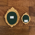 Two oval ornate gold frames and dark green textured centers, displayed on a brown wood plank floor. Each piece has a small white label reading 'P. Pleasant Atelier.'