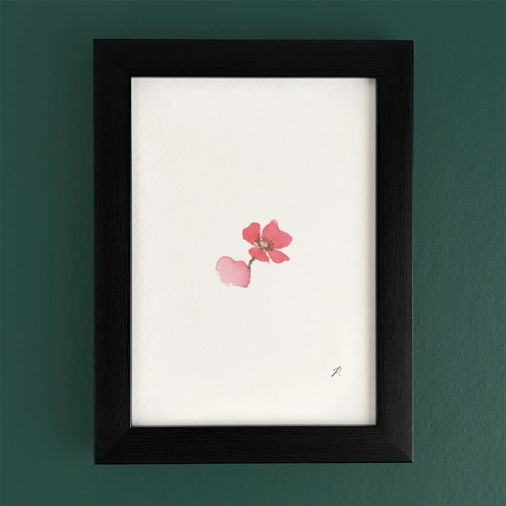 Art print in a dark wooden frame with a pink flower, set against a green wall