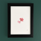 Art print in a dark wooden frame with a pink flower, set against a green wall