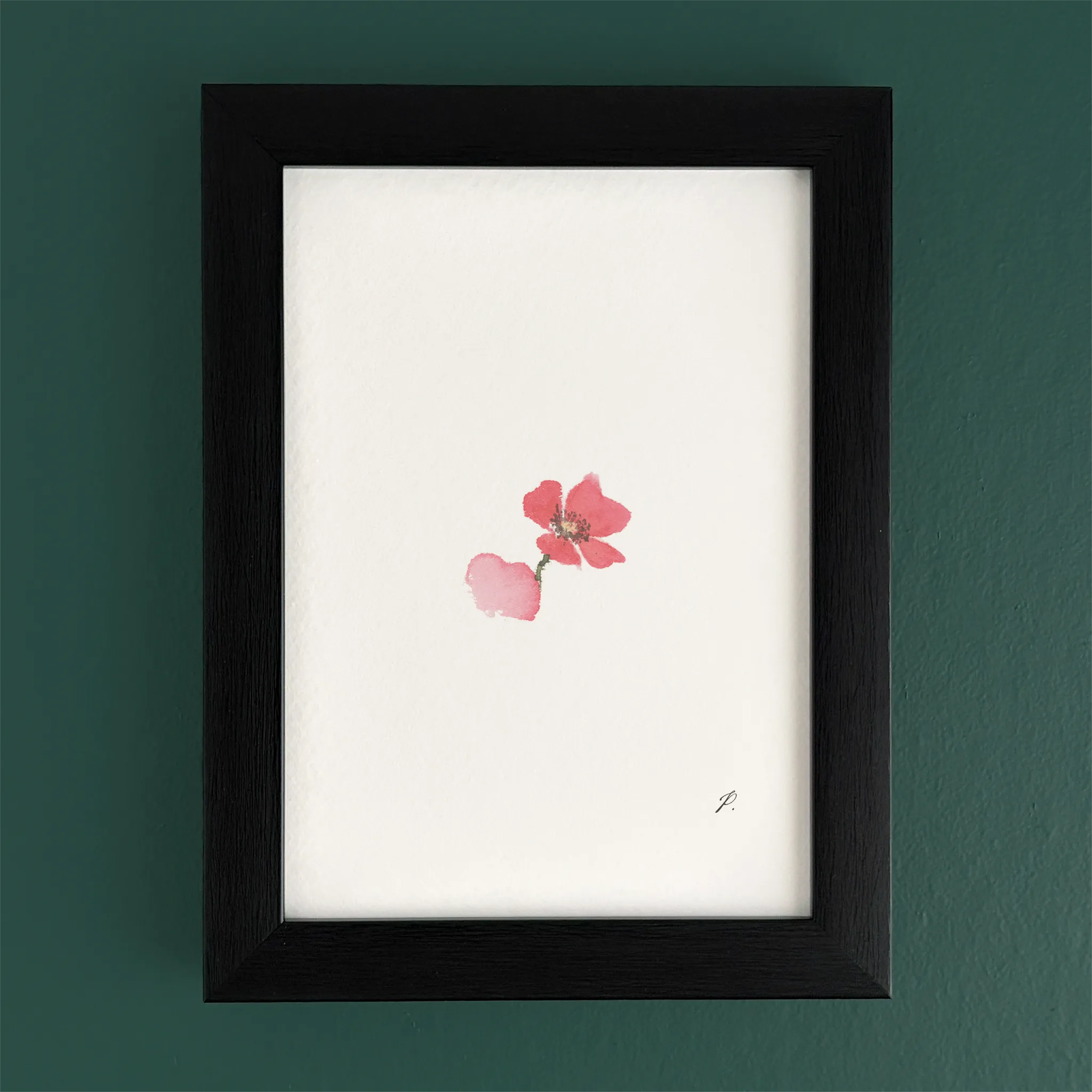 Art print in a dark wooden frame with a pink flower, set against a green wall
