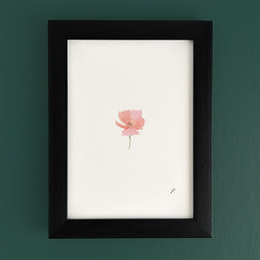 Art print in a black frame on a teal wall, with a small pink fairy flower and soft magic-style details