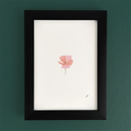 Art print in a black frame on a teal wall, with a small pink fairy flower and soft magic-style details