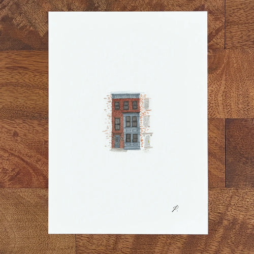 Art fairy magic illustration of a small red and blue building on a white paper sheet on a wooden table