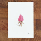 Art fairy magic character with a pink flame-like hair tuft on a white sheet over a wooden table