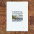 Art print on a white page showing a watercolor fairy tale style seascape with a small lighthouse and trees